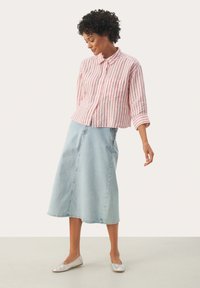 Rød og hvid stribet skjorte med knapper og krave, parret med en lyseblå denimnederdel. Modellen har sølvfarvede ballet-flade sko på.