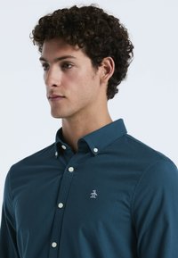 Teal knopenoverhemd met een kraag, lange mouwen en een klein wit pinguïnlogo geborduurd op de linkerborst.