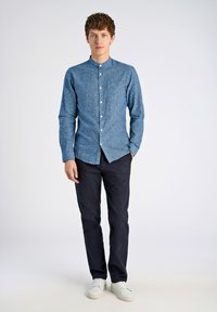 Camicia a maniche lunghe blu, a fantasia, con colletto cinese, indossata con pantaloni blu scuro e scarpe da ginnastica bianche. Tessuto liscio, design aderente.