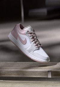 Baskets en cuir blanc avec des accents rose pâle, perforations circulaires sur le bout, et semelle en caoutchouc rose. Présente un logo swoosh bien en évidence sur le côté.