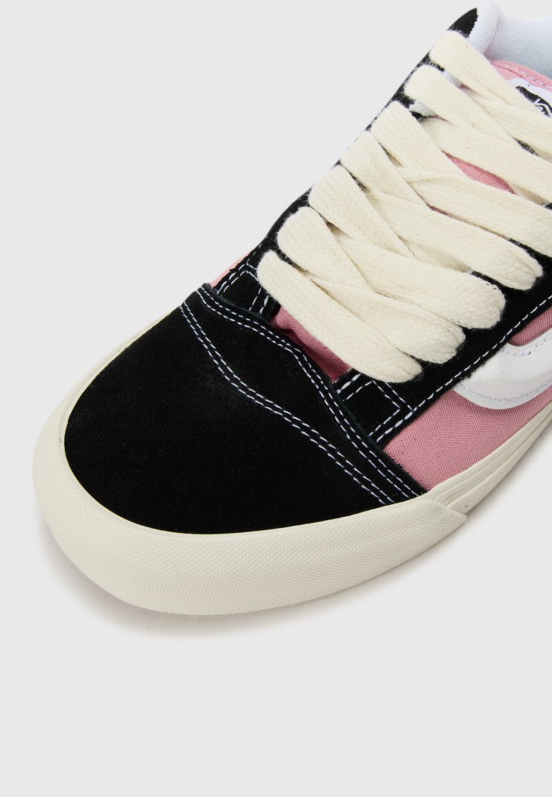 Zwarte suede en roze canvas sneaker met een wit logo, crèmekleurige veters en een dikke witte rubberen zool met een gestructureerde afwerking.