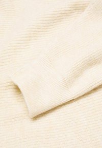 Pull en tricot couleur crème avec une texture côtelée, présentant un poignet replié et un tissu léger et doux affichant de subtiles variations de teinte.