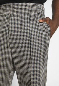 Tkané kalhoty s námořnickým a béžovým vzorem houndstooth, slim fit s bočními kapsami, vyrobené z texturované tkaniny pro zvýraznění detailů.