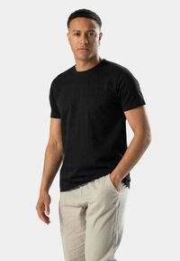 Sort bomulds T-shirt med korte ærmer, rund hals og afslappet pasform, parret med lyse beige bukser. Enkelt, glat tekstur.