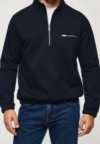 Maglione blu navy realizzato in tessuto morbido, con mezzipollo frontale, collo alto e tasca sul petto con zip. Polsini a costine.