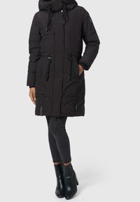 Sort puffet jakke med hætte, justerbar talje, lynlåslommer og quiltet design. Kombinationen med mørke, stramme jeans og sorte hælede støvler.