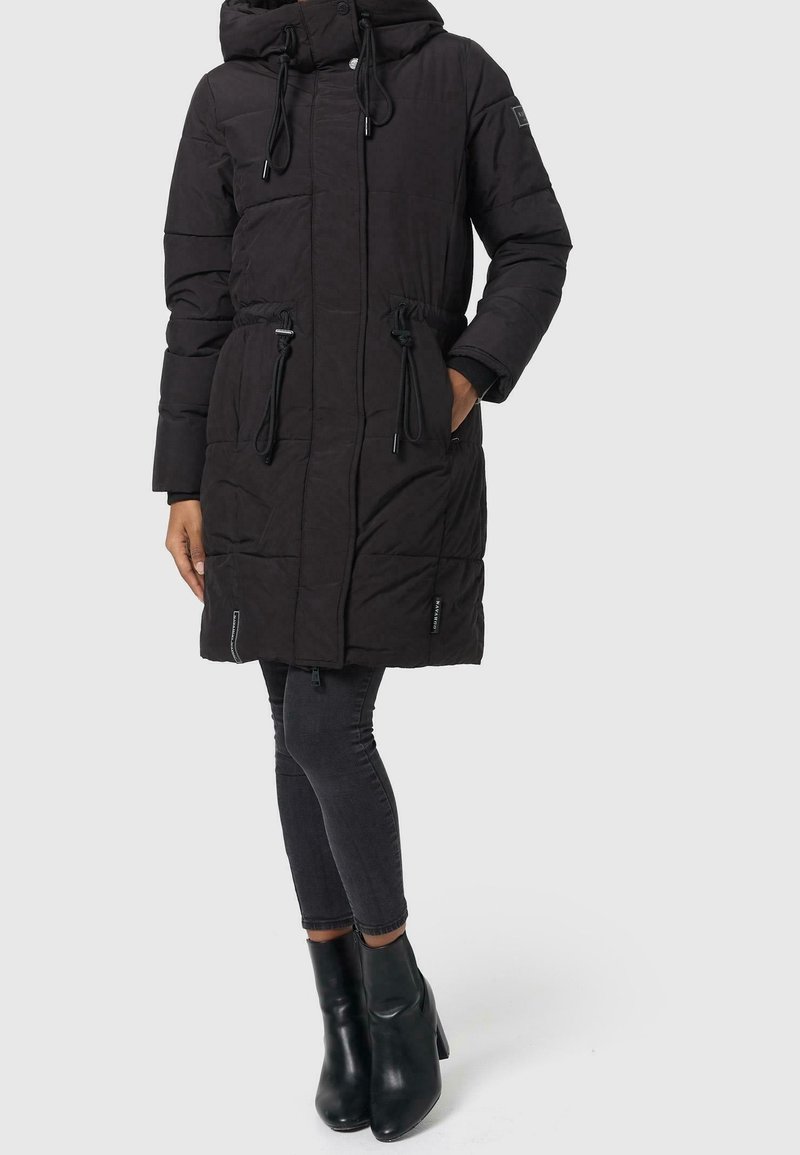 Sort puffet jakke med hætte, justerbar talje, lynlåslommer og quiltet design. Kombinationen med mørke, stramme jeans og sorte hælede støvler.