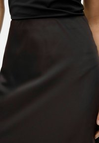 Jupe en satin noir avec une texture lisse. Dotée d'une taille ajustée et d'une silhouette droite, atteignant le milieu du mollet.