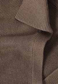 Primer plano de tela marrón tejida doblada que muestra patrones detallados de puntos acanalados y texturizados.