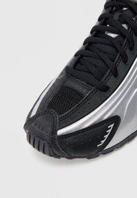 Czarne buty sportowe z srebrnymi akcentami, z siateczkowej i syntetycznej cholewki, teksturowaną podeszwą i wzmocnionym noskiem. Posiadają zapięcie na sznurówki i otwory wentylacyjne.