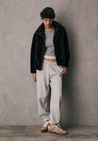 Brun fleece zip-up jakke, grå tætsiddende top, grå sweatpants, beige sneakers. Bløde teksturer, afslappet pasform og neutrale farver.