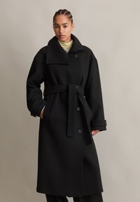 Zwarte wollen trenchcoat met een grote kraag, zijzakken en een tailleband, met knoopsluiting en een relaxte pasvorm.