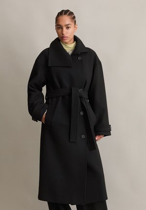 Schwarzer wollener Trenchcoat mit großem Kragen, Seitentaschen und Taillengürtel, mit Knopfverschlüssen und lässigem Schnitt.