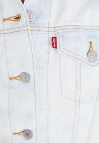 Svijetloplava traper jakna s srebrnim gumbima, žutim šavovima i malom crvenom Levi's etiketom na prednjoj džepu.