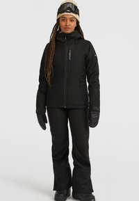 Veste de neige noire avec fermeture éclair, dotée d'une capuche et de plusieurs poches, associée à un pantalon et des gants noirs assortis. Texture lisse.