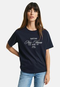 Námořnická modrá bavlněná tričko s bílým textem, který zní "GANT 1949 New Haven Sailing Crew 06516 CT. USA," s volným střihem.
