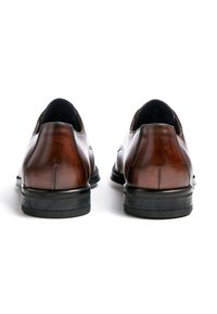 Scarpe di pelle marrone con finitura liscia, caratterizzate da una punta arrotondata e robuste suole in gomma nere. Vista posteriore che mostra i dettagli delle cuciture e i contorni del design.