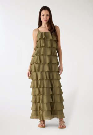 Abito lungo verde oliva senza maniche con più volant sovrapposti, tessuto fluente e orlo dritto; indossato con sandali bassi.