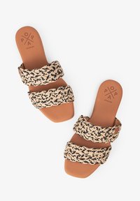 Sandalias planas con dos amplias correas trenzadas en tonos naturales con acentos en negro, colocadas sobre una plantilla marrón y suave. Logo visible en la plantilla.