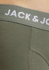 Khaki zöld alsónemű, puha elasztikus derékpánttal, amelyen a "JACK & JONES" felirat fehér színben olvasható. Finom bordázott textúra és varrott varratok jellemzik.