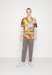 Cămașă cu mâneci scurte, multicoloră, cu modele abstracte, asociată cu pantaloni gri și teniși albi. Țesătură netedă, croială lejeră.