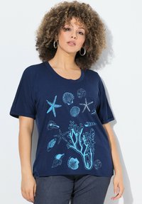 Námořnická modrá tričko vyrobené z měkké tkaniny, s světle modrými mořskými motivy včetně mušlí, hvězdic a korálů. Krátké rukávy.