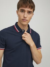 Marineblå polo shirt lavet af bomuld, med en to-knap placket og krave, samt røde og hvide stribede detaljer på ærmerne.