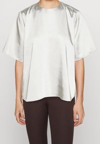 Haut court en satin argenté à manches courtes avec un col rond. Coupe ample et texture lisse, avec un léger éclat et des fentes latérales pour faciliter les mouvements.