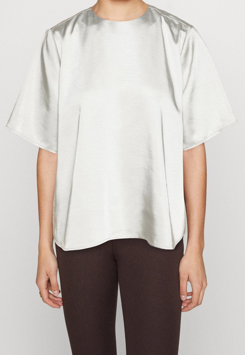 Haut court en satin argenté à manches courtes avec un col rond. Coupe ample et texture lisse, avec un léger éclat et des fentes latérales pour faciliter les mouvements.