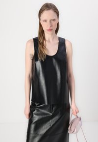 Black leather sleeveless top with a scoop neckline and smooth texture, paired with a matching leather skirt, holding a light pink bag.