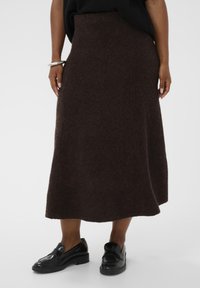 Rjava, srednje dolga, a-linijska krila iz mehkega, teksturiranega blaga. Ima visok pas in enakomeren rob, v kombinaciji s črnimi čevlji.