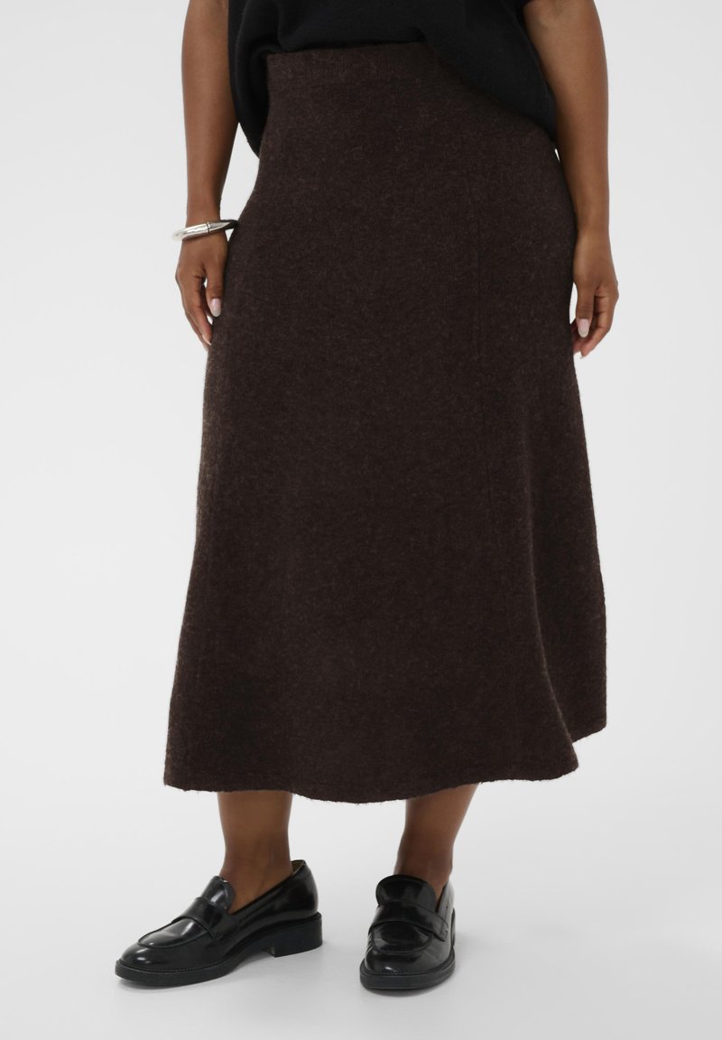 Rjava, srednje dolga, a-linijska krila iz mehkega, teksturiranega blaga. Ima visok pas in enakomeren rob, v kombinaciji s črnimi čevlji.