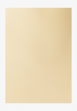 Žena v světle žlutých kalhotách s předními kapsami a stříbrným zapínáním, stojící na jednobarevném bílém pozadí.