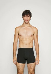 Černé látkové boxerky, přiléhavý střih, hladká textura, délka do poloviny stehna, nošeny mužským modelem, na neutrálním pozadí.