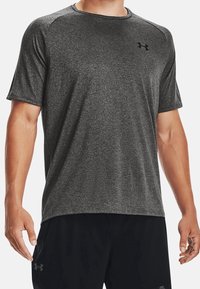 Camiseta deportiva de manga corta hecha de tela gris oscuro que absorbe la humedad, con cuello redondo y acabado sutilmente texturizado. Presenta un logo en el pecho.
