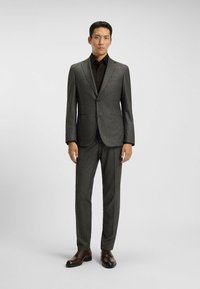 Grijs visgraatpak met een gelapyte revers, zwart overhemd en bruine leren schoenen. Perfecte pasvorm, gestructureerde stof en een strak ontwerp.