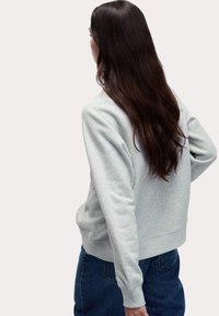 Felpa grigio chiaro in morbido tessuto testurizzato, con collo a giro e polsini a coste, abbinata a jeans di denim blu scuro.