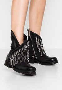 Svarta läderankelstövlar med silvermetallaccenter, utrustade med en unik lagerdesign och en sidodragkedja för enkelt påtagande. Texturerad läderfinish.