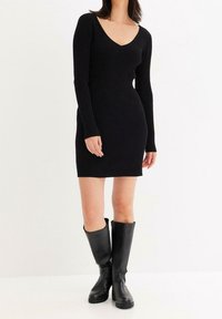 Svart ribbad stickad klänning med djup V-halsringning och långa ärmar, ihop med knähöga svarta läderstövlar med kraftig sula.