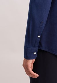 Marineblauwe overhemd met lange mouwen, voorzien van knopenmanchetten, een gestructureerde stof en een rechte zoom. Close-up van de mouw en hand.