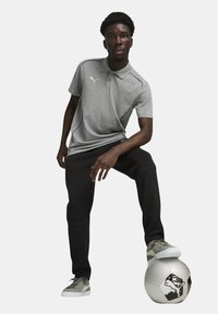 Grå polo skjorte med krave, slank design og sølv detaljer, parret med sorte bukser og grå sneakers, placeret ved siden af en fodbold.