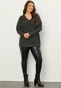 Dunkelgrauer Strickpullover mit V-Ausschnitt, langen Ärmeln und Glitzerelementen, kombiniert mit schwarzen Leggings aus Kunstleder und Ankle Boots.