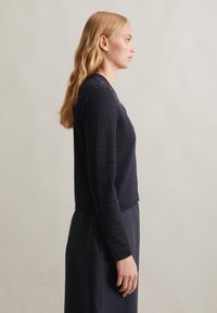 Granatowy sweter dzianinowy o teksturowym wzorze, z długimi rękawami, okrągłym dekoltem i zapięciem na guziki, noszony na dopasowanej sukience.
