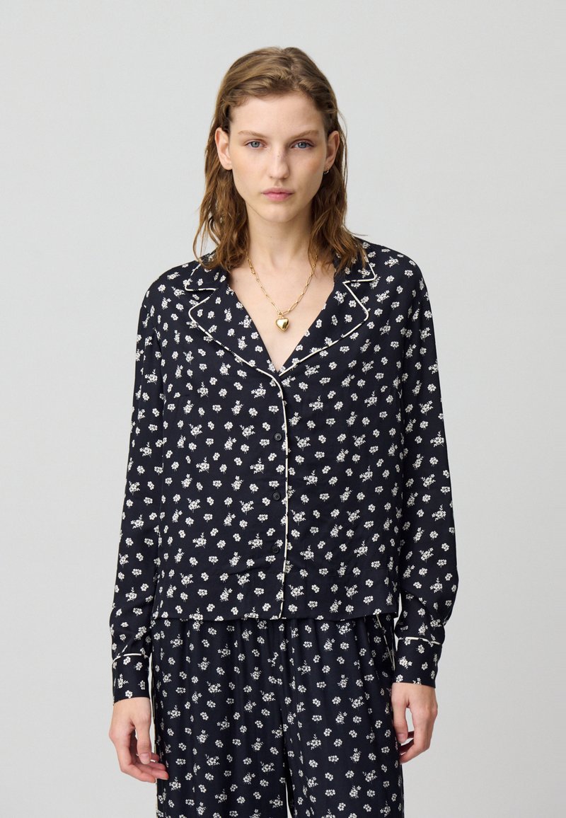 Completo pigiama navy con motivo floreale bianco, dotato di camicia con bottone, colletto e bordi a contrasto in pipetta. Tessuto morbido, maniche lunghe.