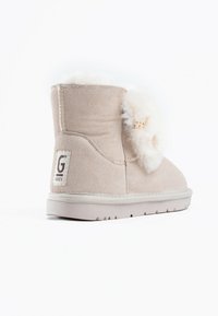 Bottine en suédine beige avec bordure en fourrure texturée, bout rond et semelle en caoutchouc. Présente un patch logo sur le talon et des coutures contrastantes.
