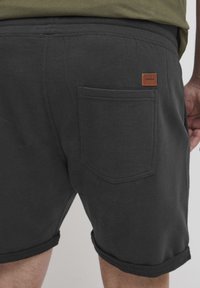 Sorte bomullsshorts med rullede oppbrett, med en baklomme og en liten brun lærmerke på livet.