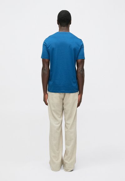 Niebieski T-shirt z krótkim rękawem i okrągłym dekoltem, w zestawie z jasnobeżowymi, szerokimi spodniami. Gładka faktura, casualowy krój.