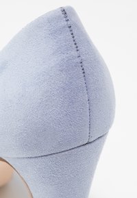 Gros plan sur une chaussure à talon haut en suède bleu clair, mettant en avant l'arrière pointu et les détails de la couture.