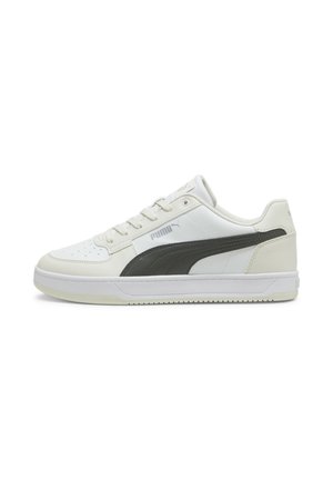 Biały niski sneaker Puma z czarnym logo w paski, wiązany na sznurówki, z gumową podeszwą, widoczny z boku na białym tle.