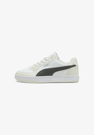 Biały niski sneaker Puma z czarnym logo w paski, wiązany na sznurówki, z gumową podeszwą, widoczny z boku na białym tle.